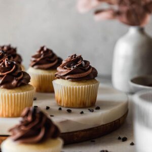A very closeup image of high altitude yellow cupcakes with chocolate buttercream on a marble cake stand with a grey background.