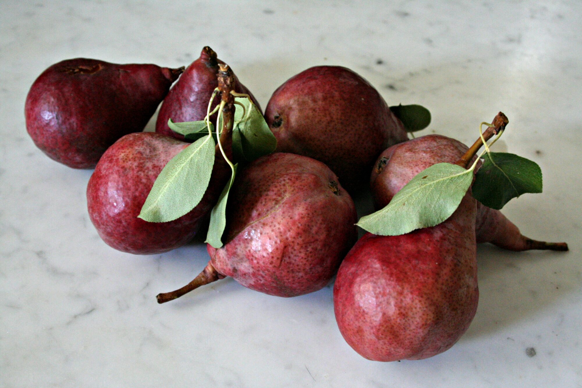 A pile of red pears on a white marble counter.