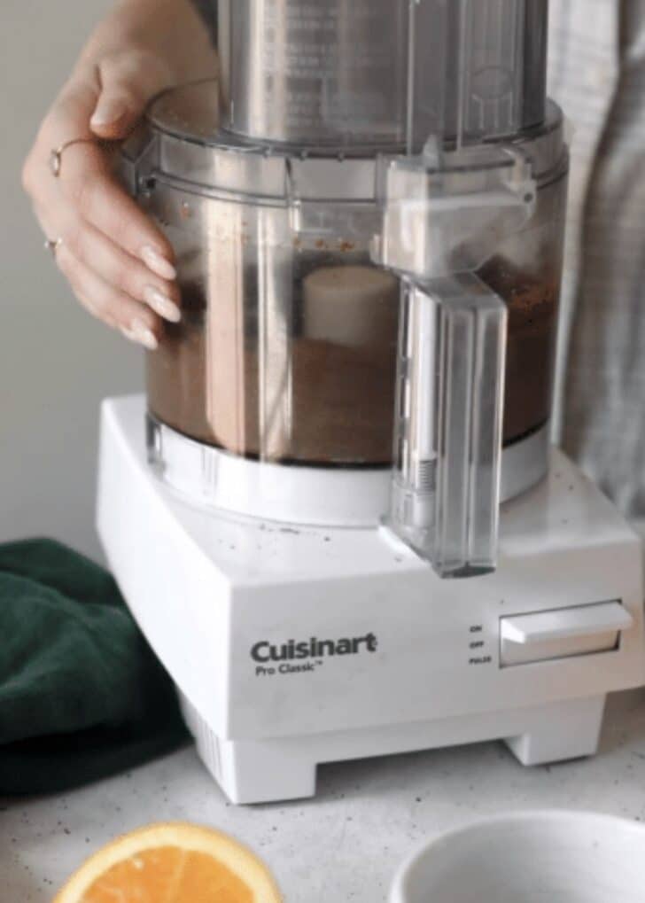 A food processor blending almond crust on a grey counter.