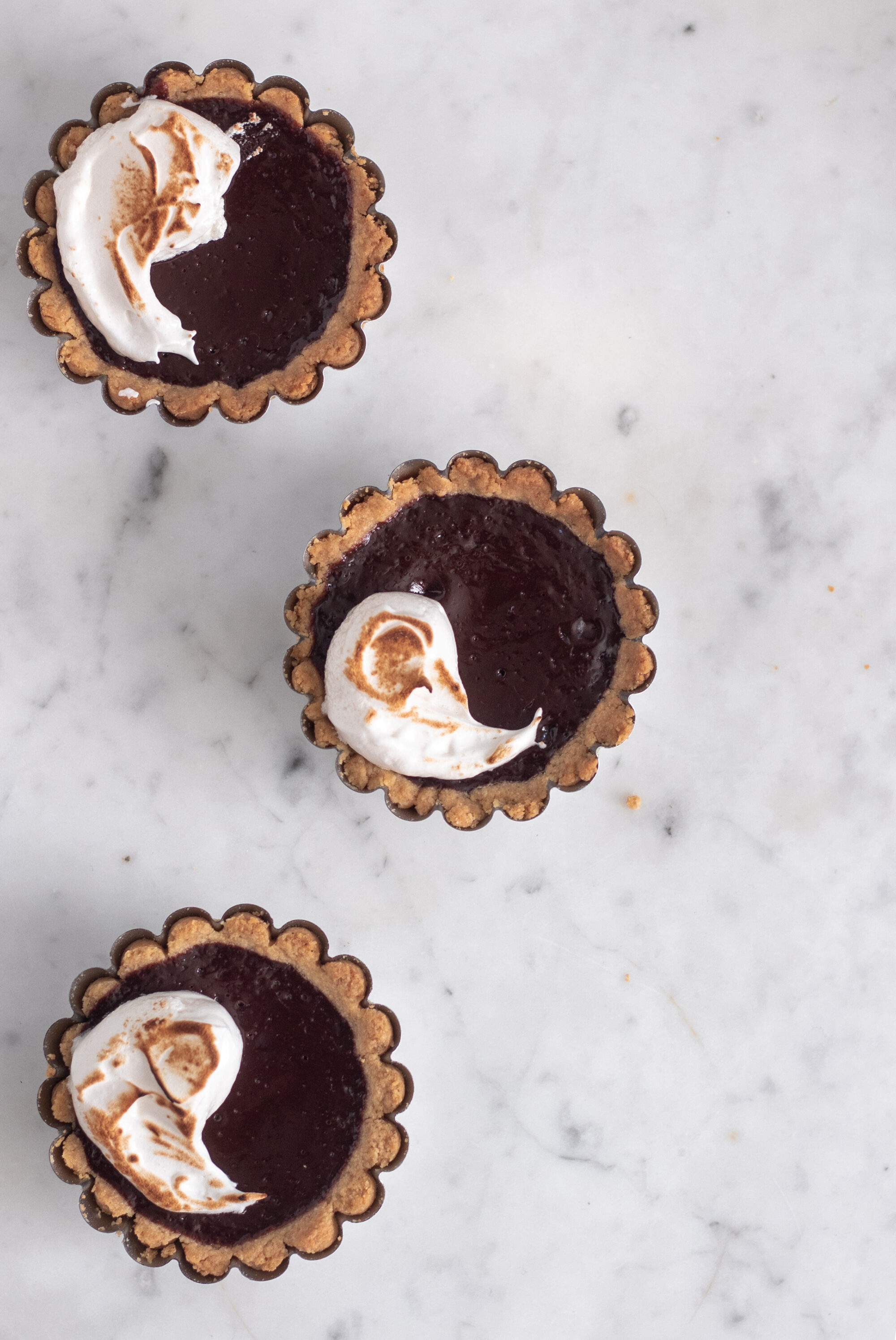 Three mini s'mores tarts in a row on a white counter.