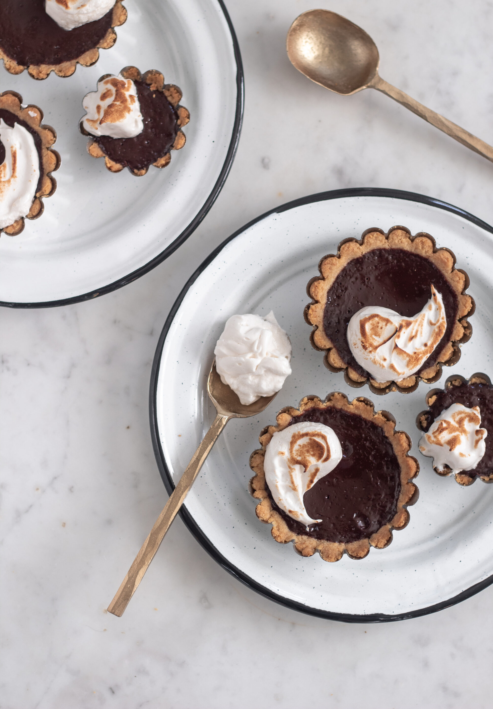 Two white plates with black rims topped with mini s'mores tarts on a marble counter.