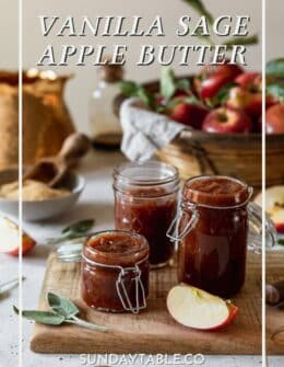 Three jars of sage apple butter on a wood board with a basket of apples and gold teapot in the background on a white counter.