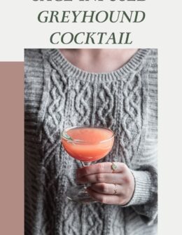 An image of a woman in a grey sweater holding a pink cocktail in a coupe glass.