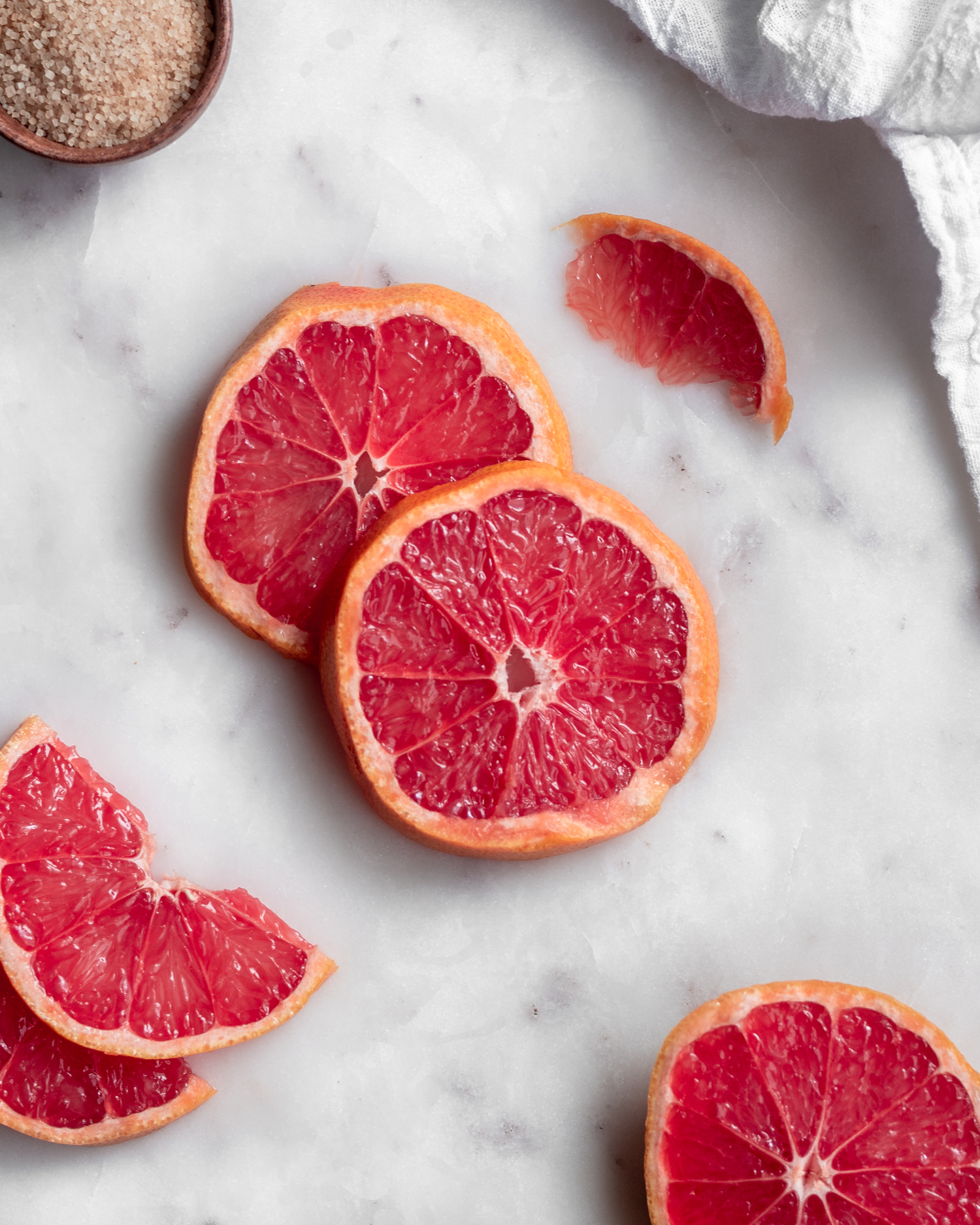 An overhead image of slices of grapefruit on a marble counter.