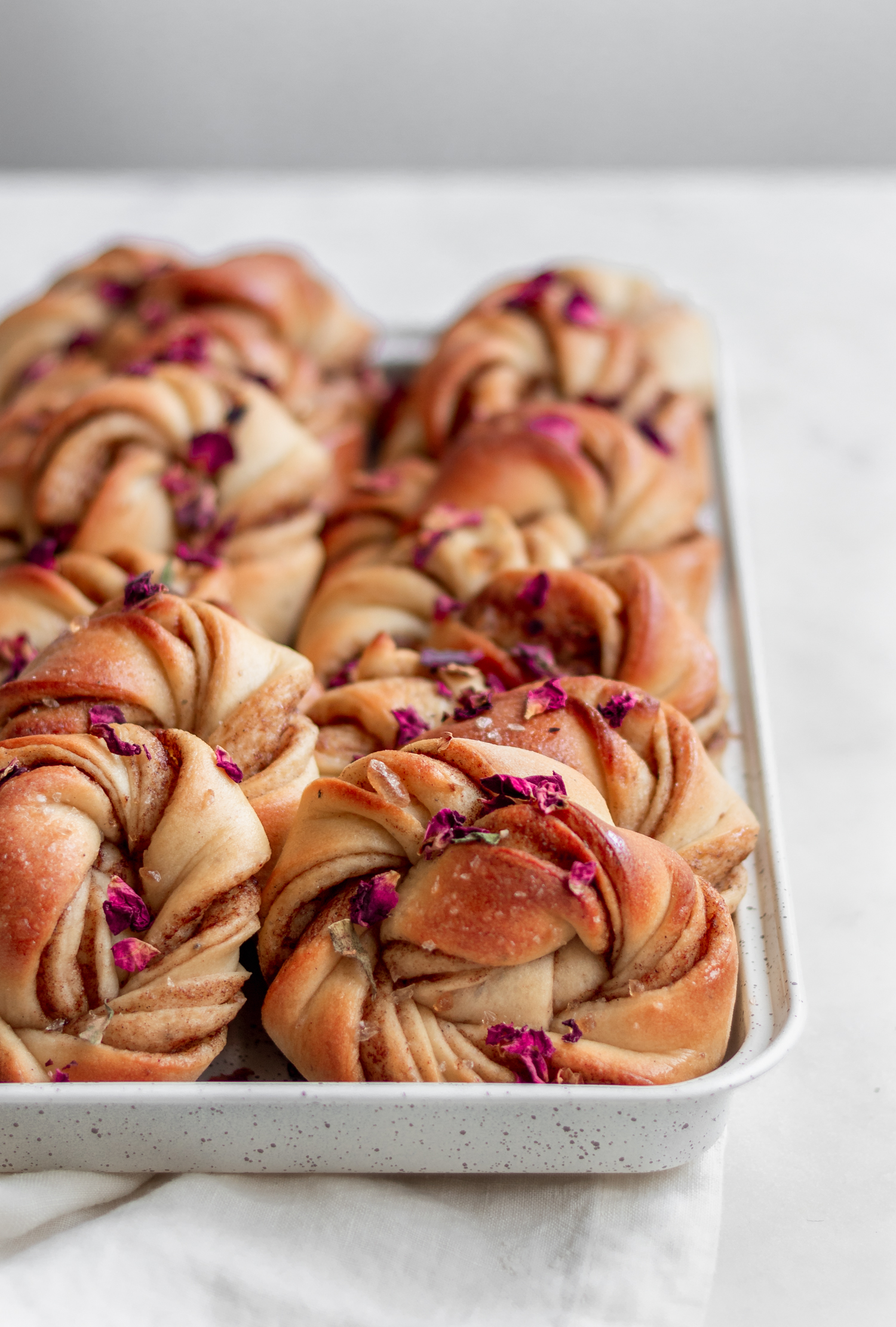 A very closeup image of rows of rose cardamom buns on a white counter.