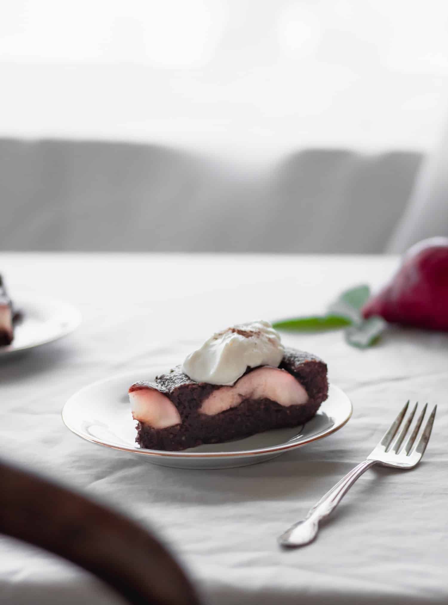 A closeup side image of a white plate with a slice of Torta Caprese on a white table cloth next to a vintage fork.