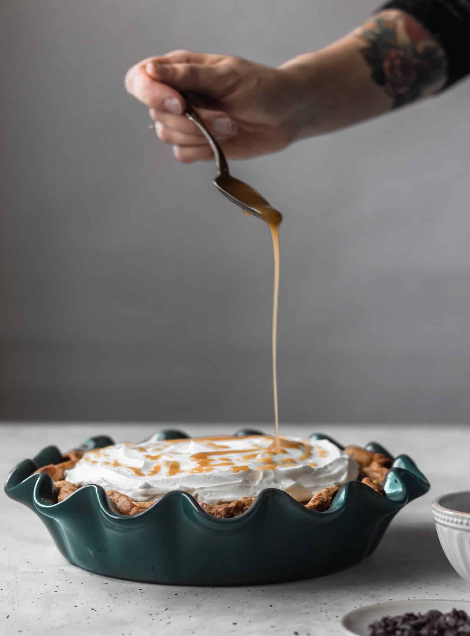 A side image of a woman drizzling bourbon butterscotch over a cocoa tart with a white background.