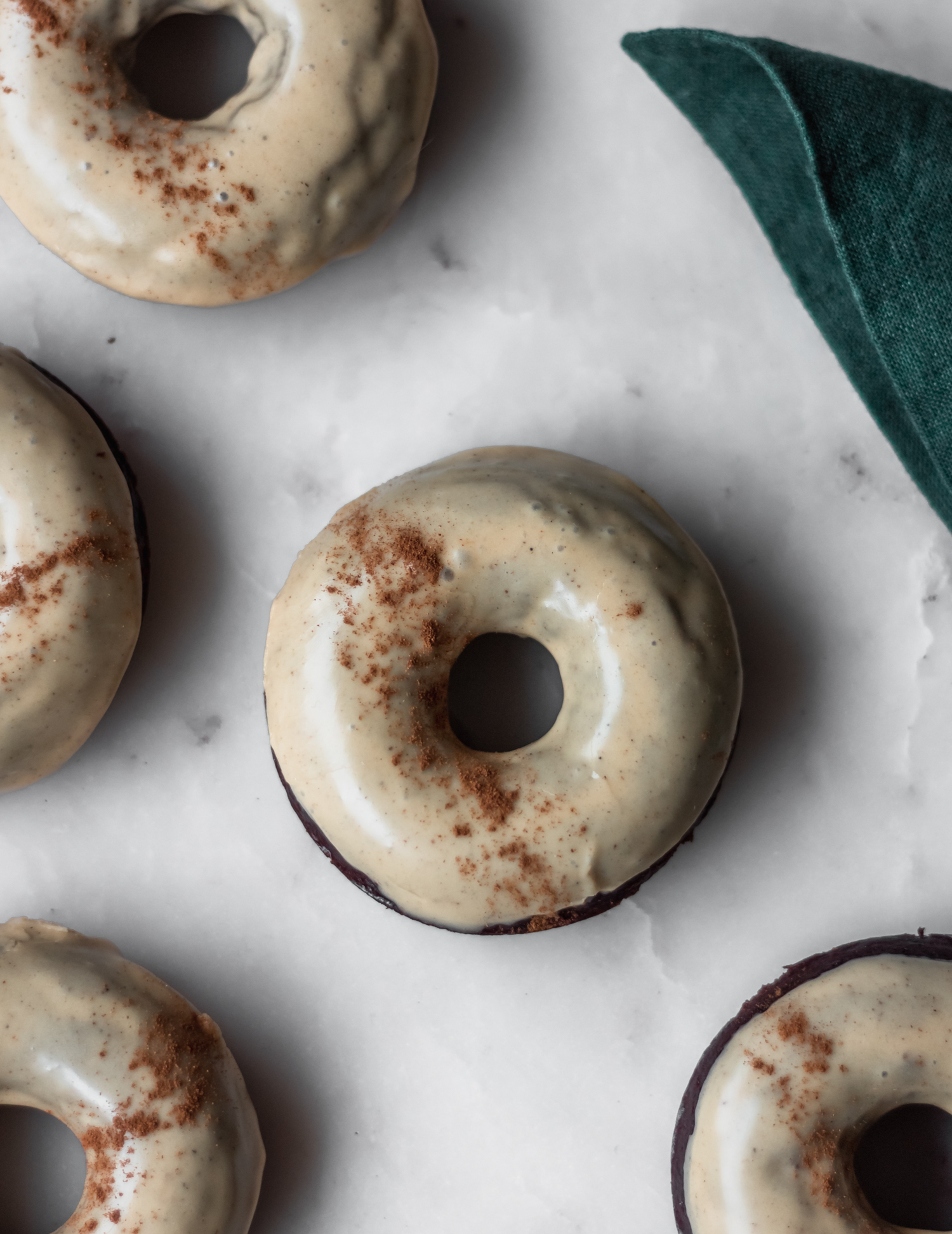 A closeup of baked chocolate donuts with chai glaze on a marble counter.