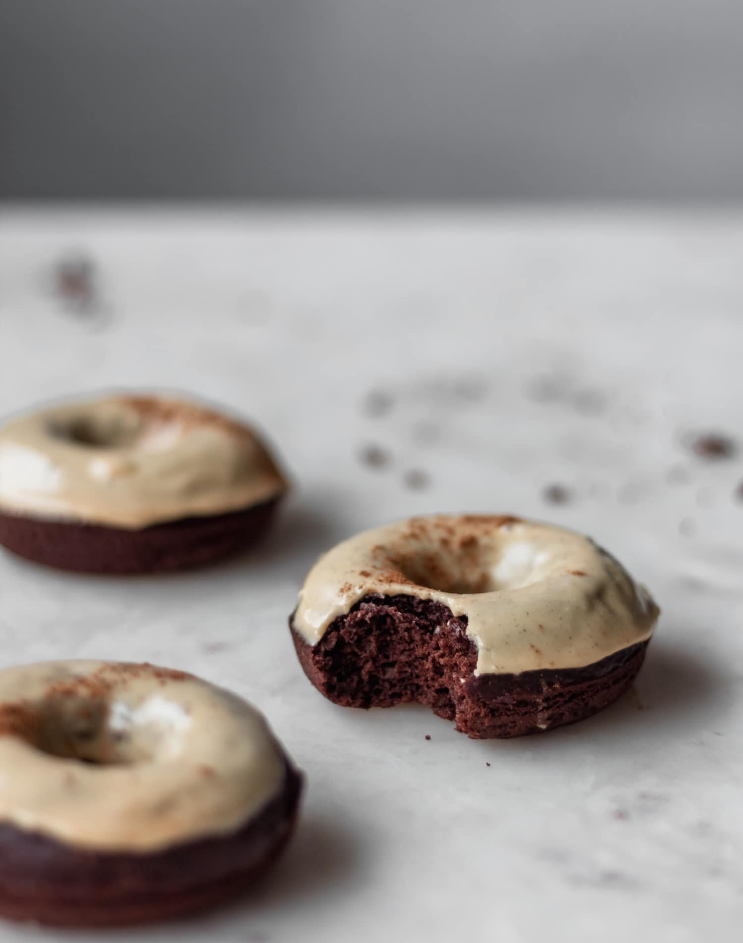 A closeup of a baked chocolate donut with chai glaze with a bite taken out of it on a white table.