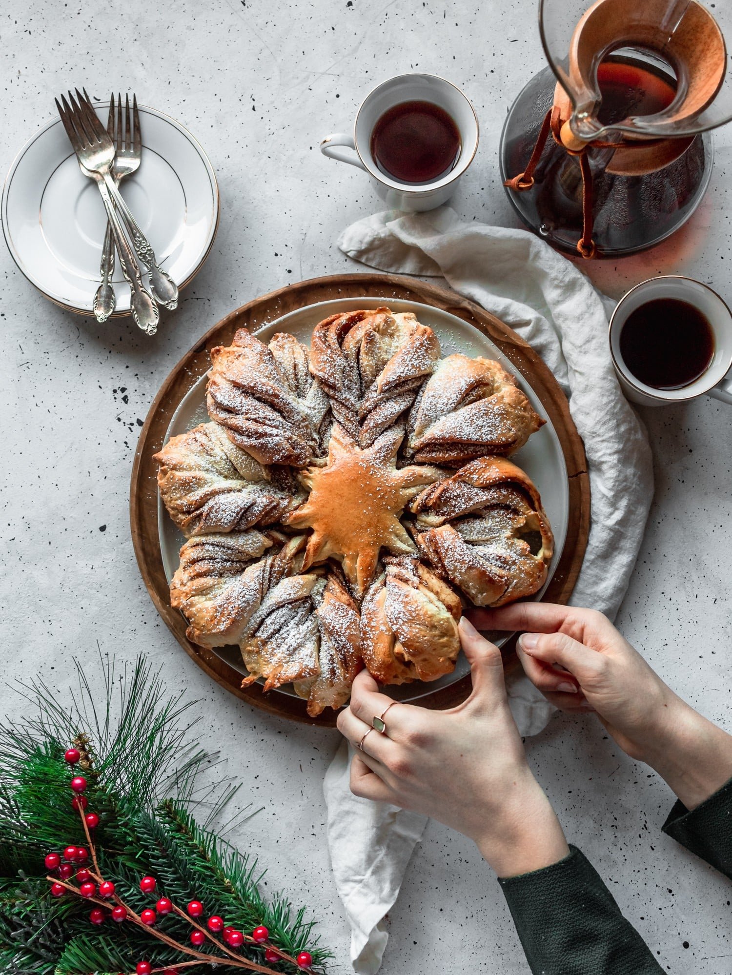 A woman pulling a piece of cookie butter cinnamon star bread on a white table next to coffee and garland.