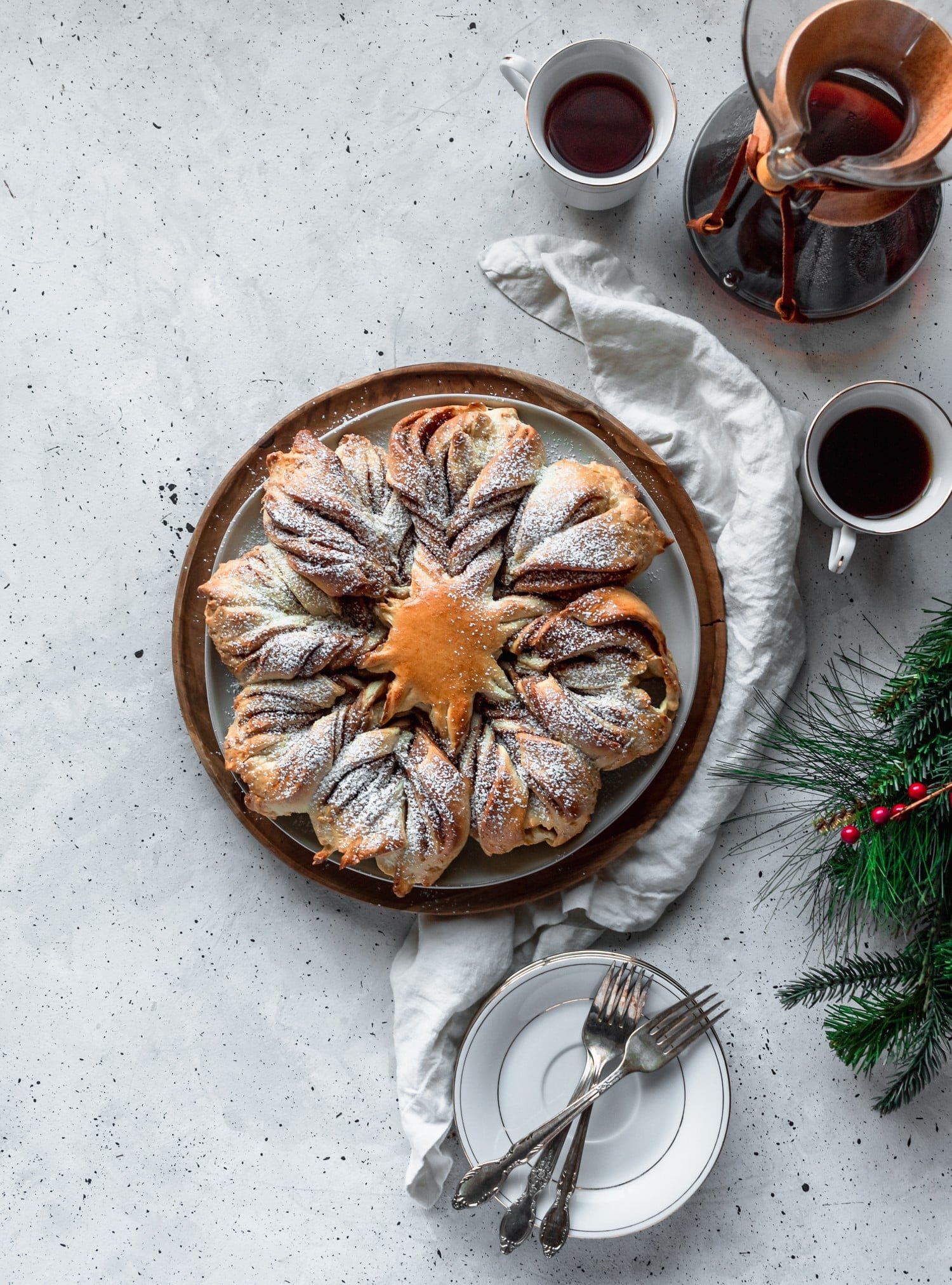 Cookie butter cinnamon star bread on a grey counter next to white plates, coffee, and garland.