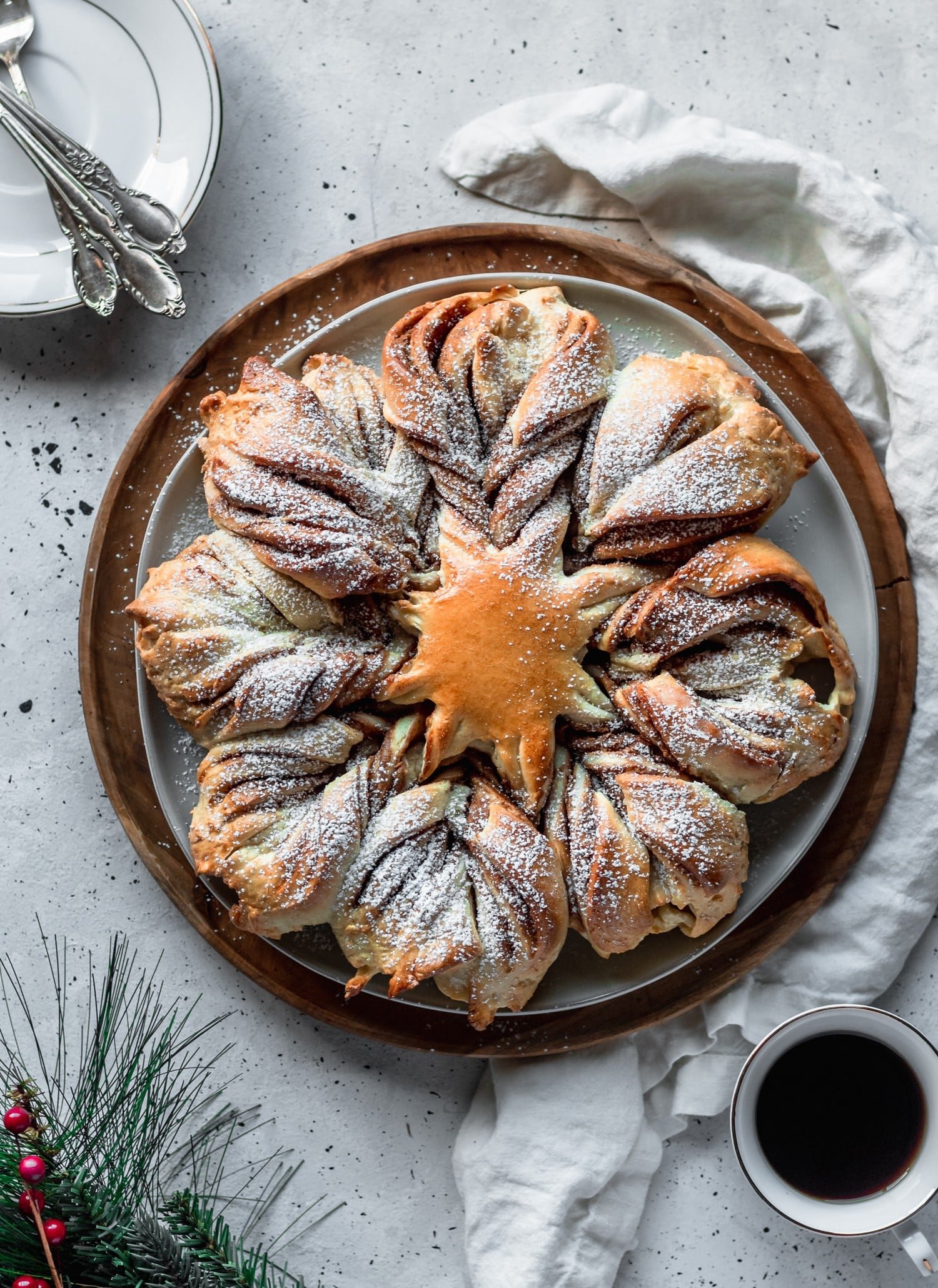 Christmas bread on a white linen next to plates and garland with a white background.