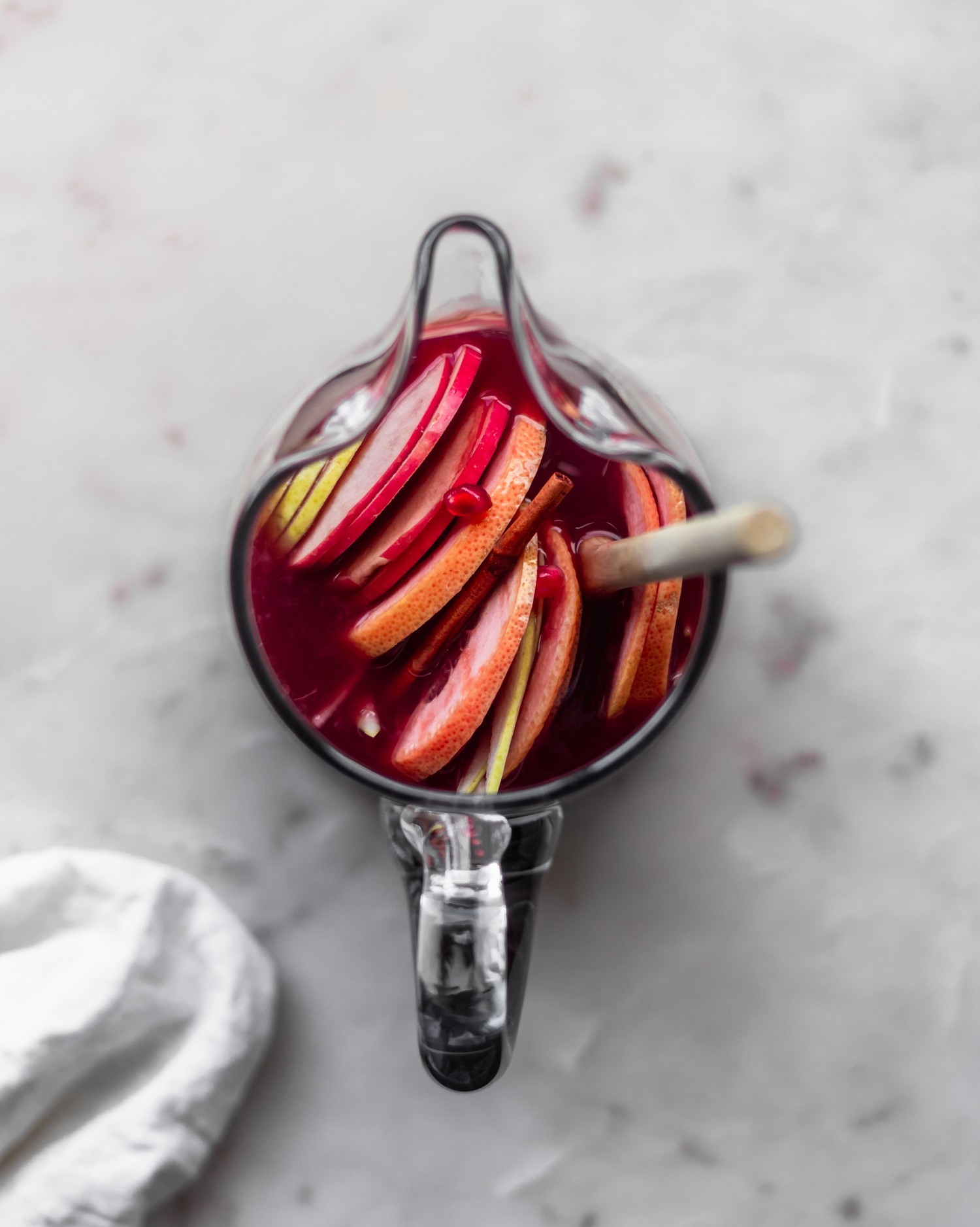 A closeup over head photo of a pitcher of red wine filled with citrus fruits, pears, and apple slices.