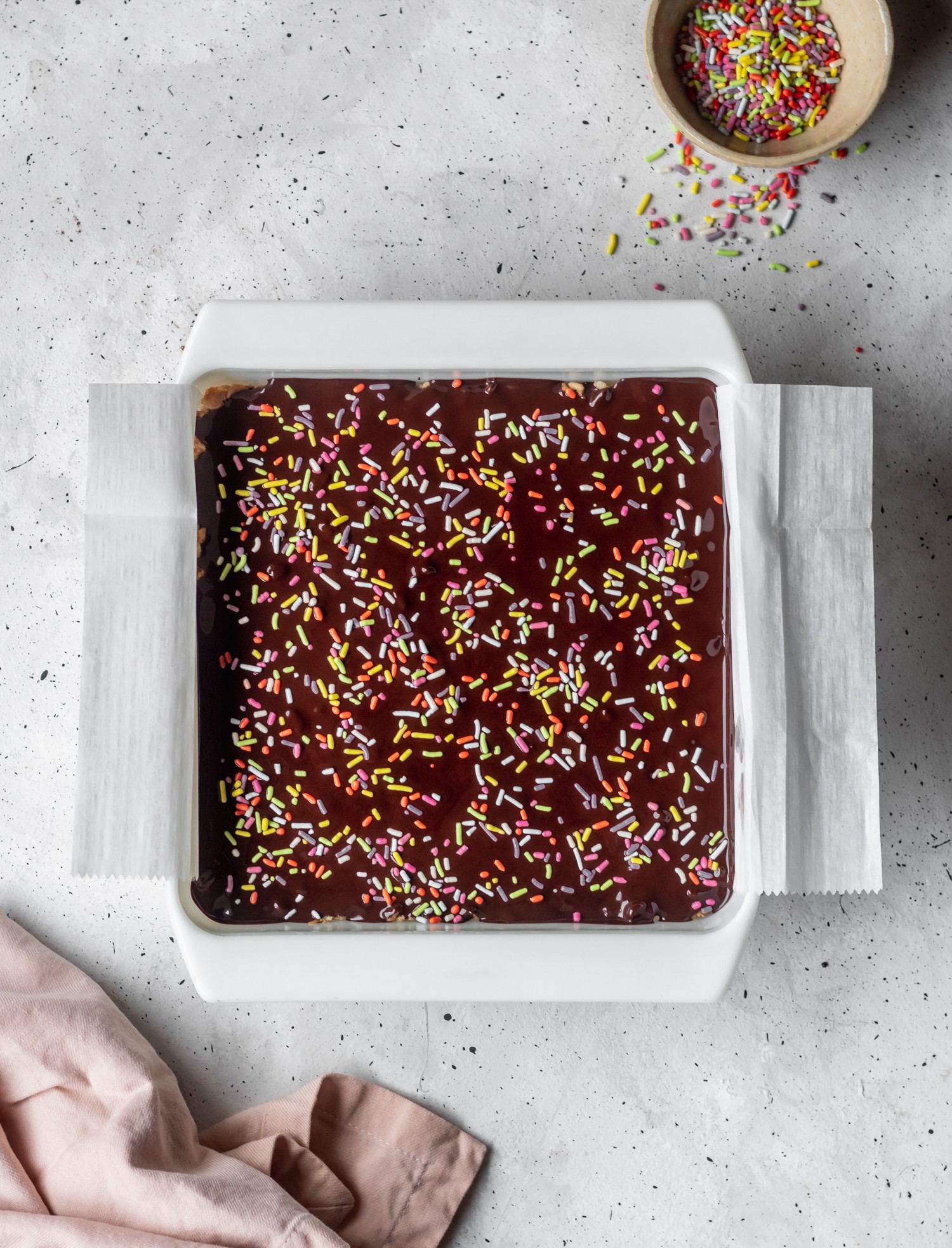 Chocolate-y dessert bars with rainbow sprinkles in a white, speckled surface.
