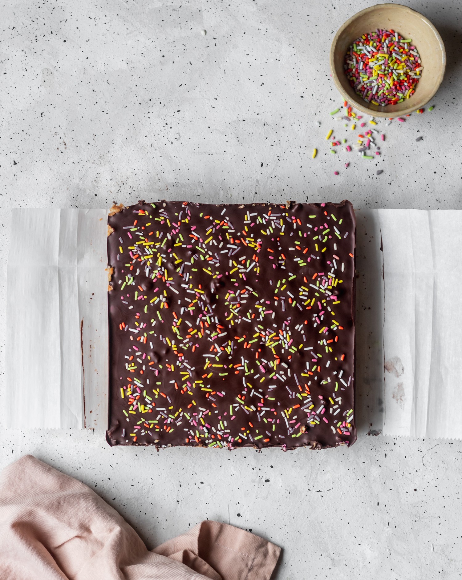 Peanut Butter Chocolate Bars with Rainbow Sprinkles placed on a white, speckled surface.