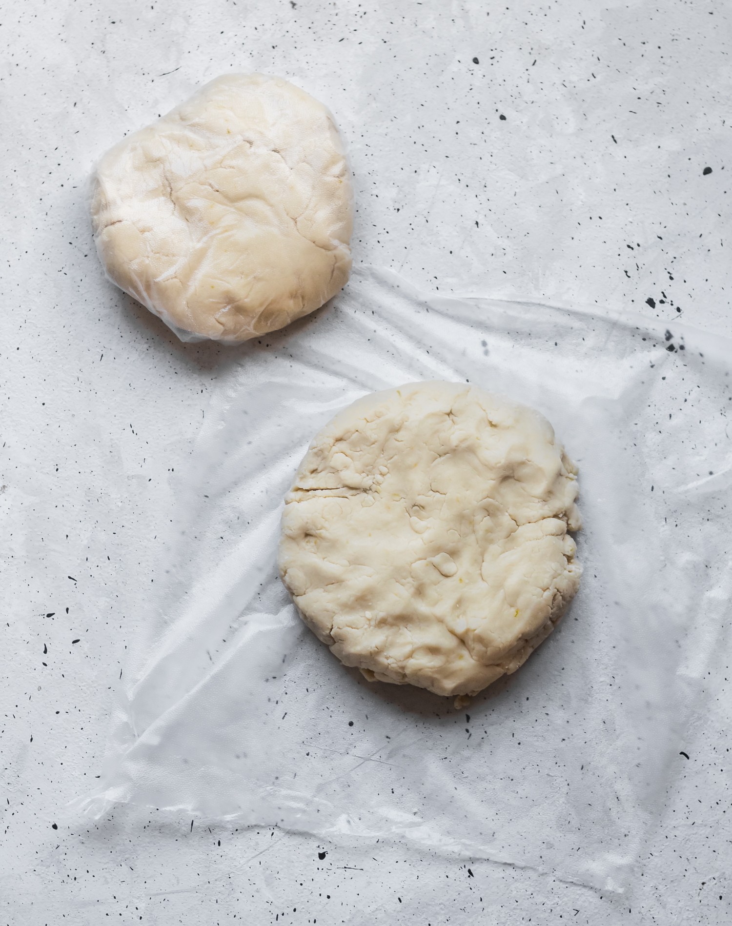 Two discs of dough wrapped with plastic sitting on a speckled table.