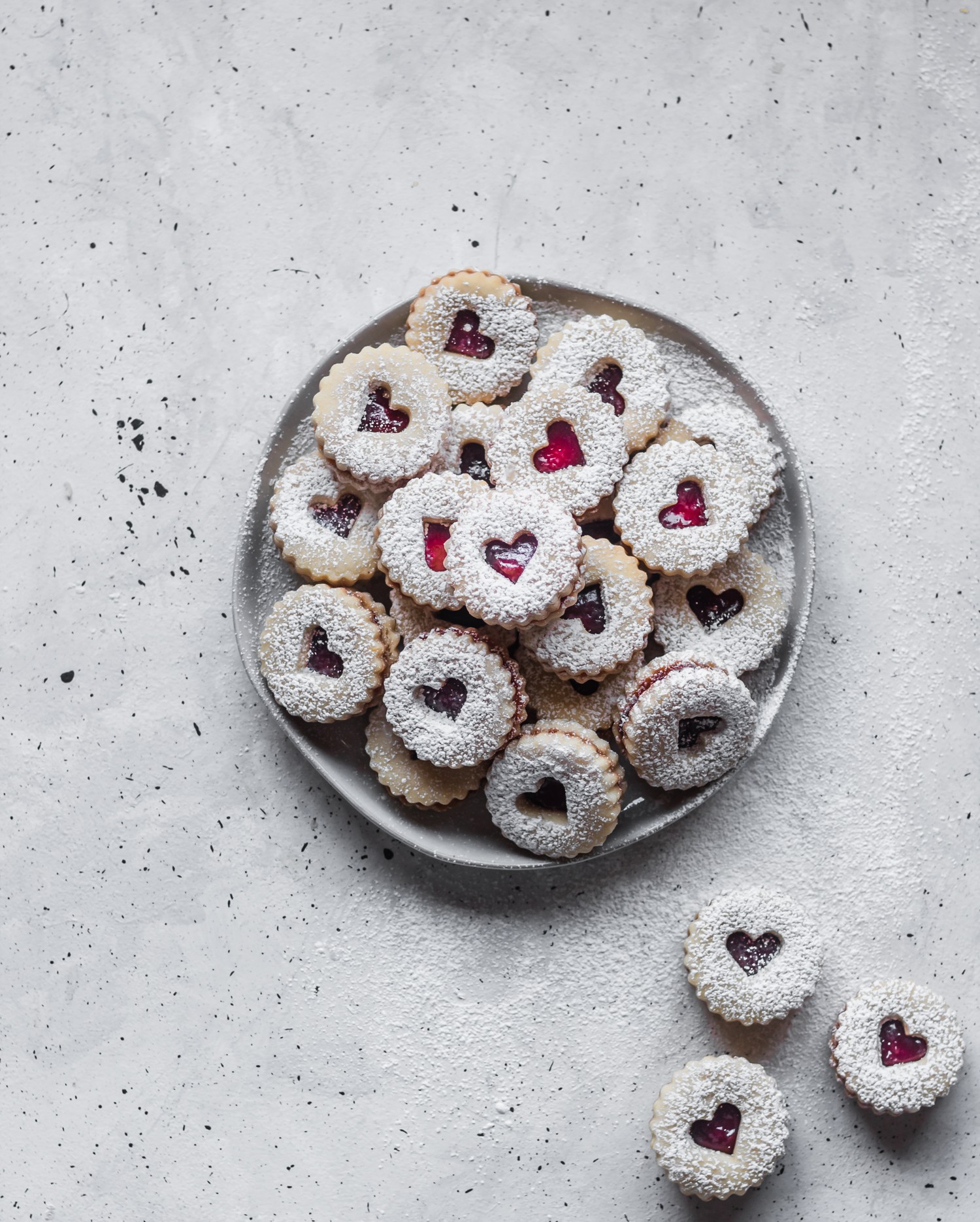 A white plate of raspberry heart cookies on a speckled background.
