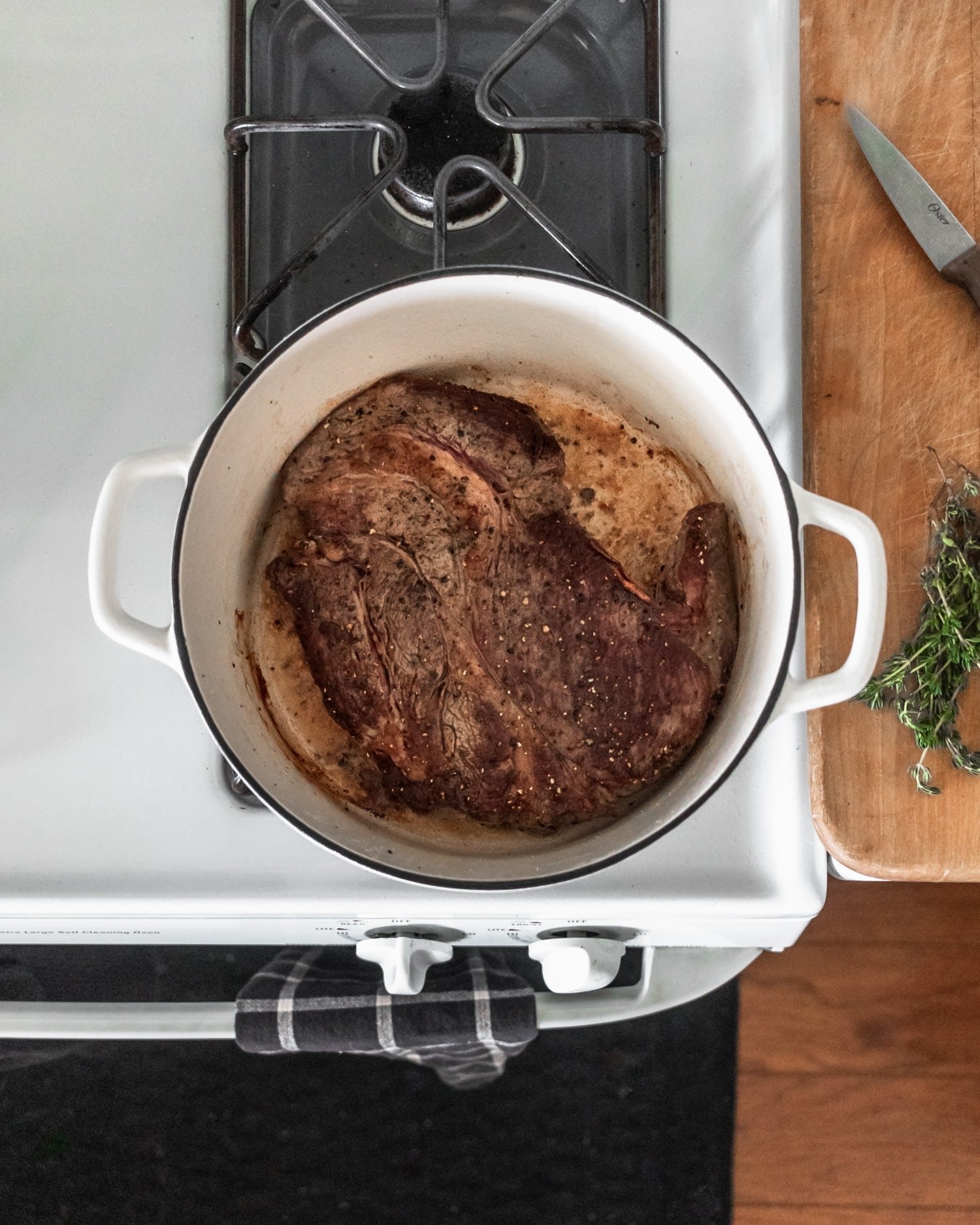 A pot of seared meat on a white stove next to a wood counter top.