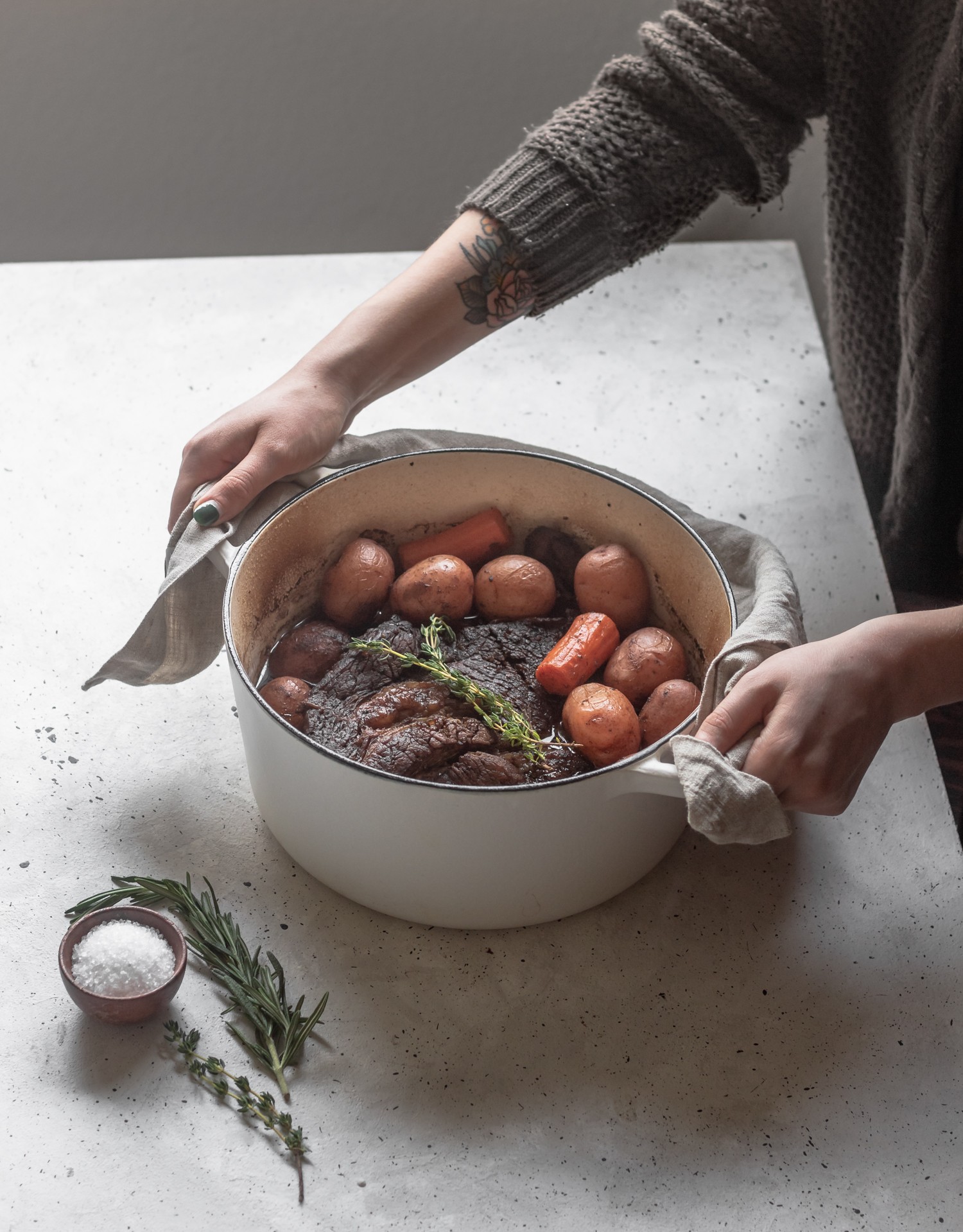A woman's hands holding a pot of beef and vegetables on a white background.