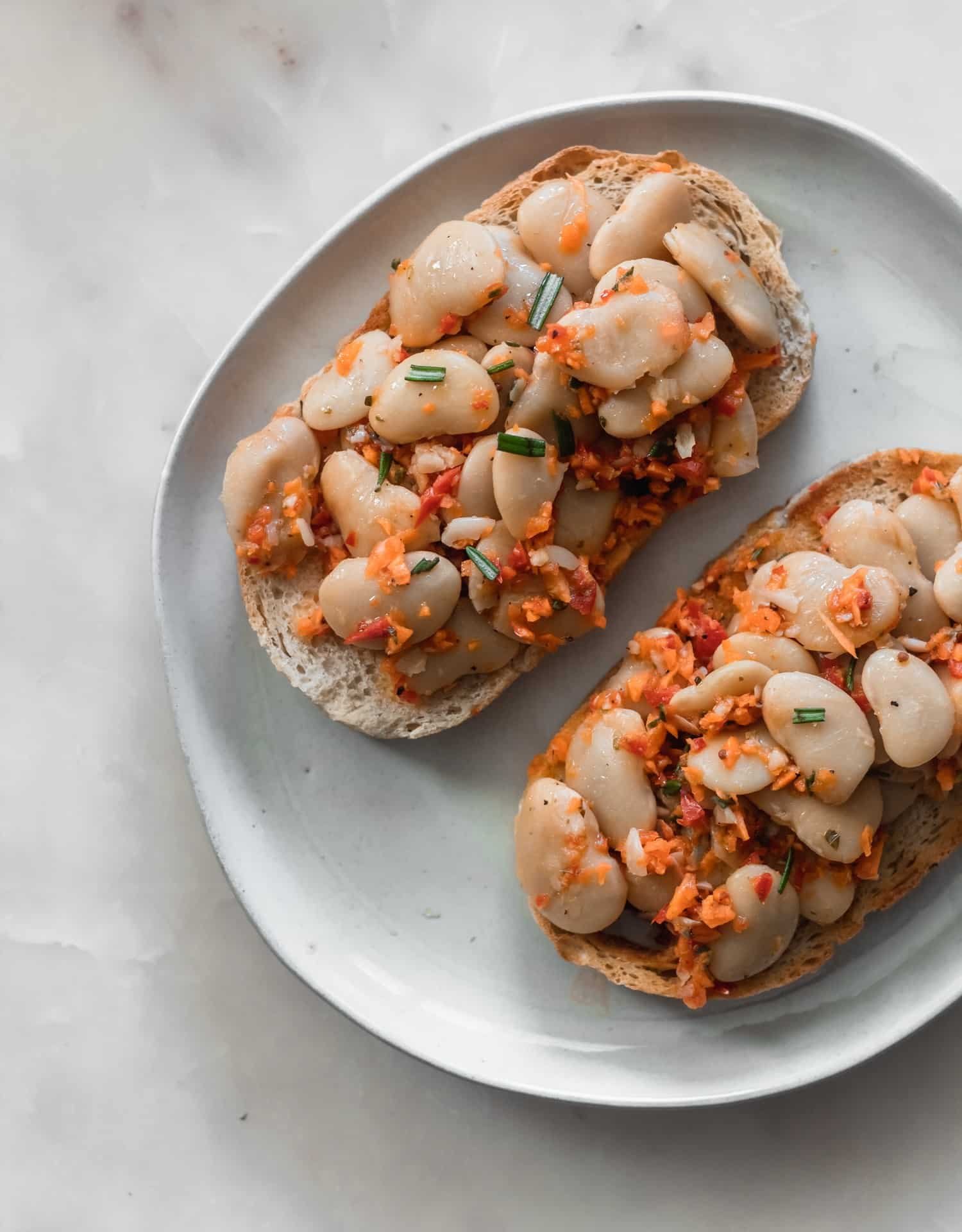 A closeup of white beans on toast sitting on a white plate on a marble counter top.