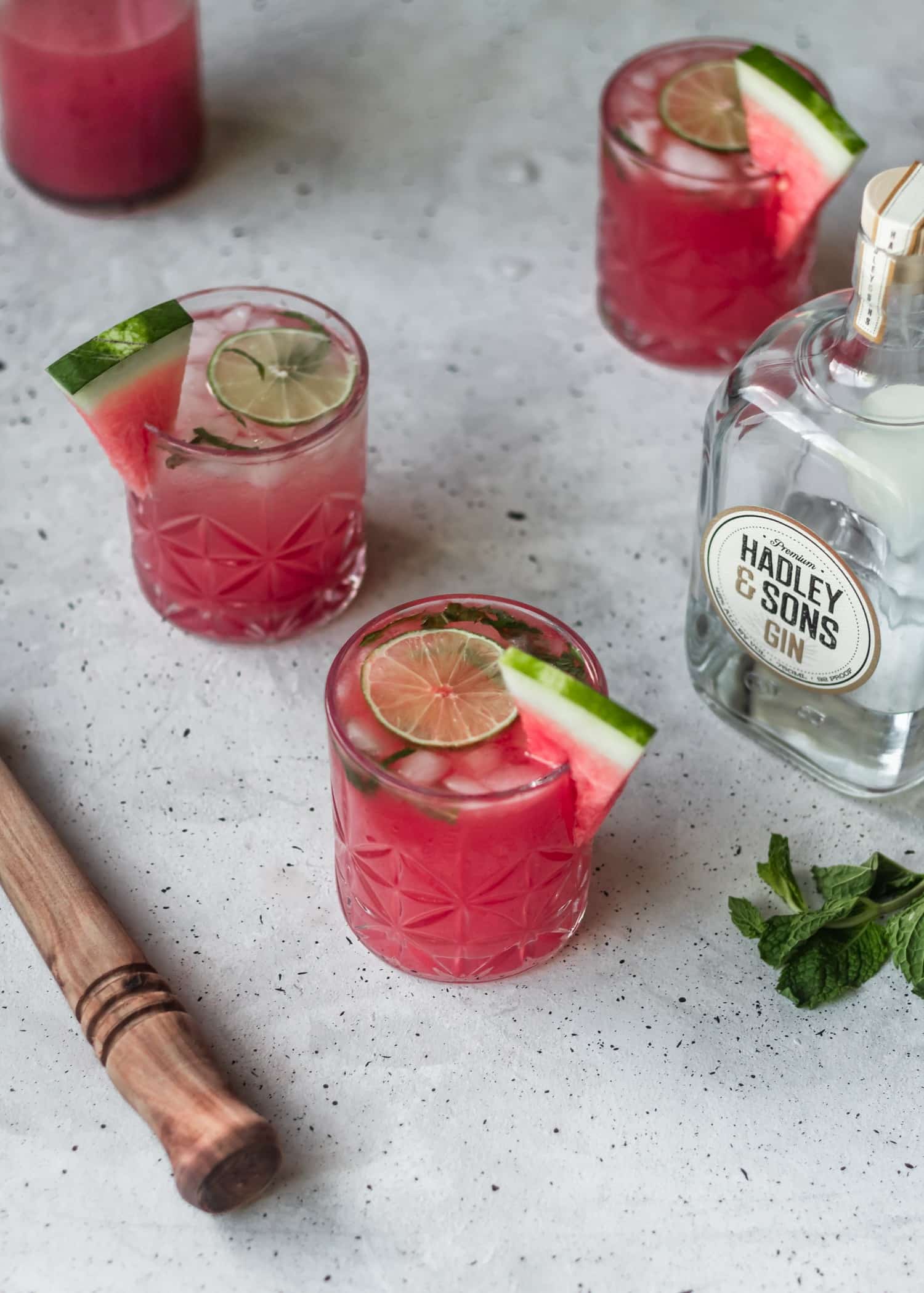 Three watermelon gin fizz cocktails on a white counter next to mint and a bottle of gin.