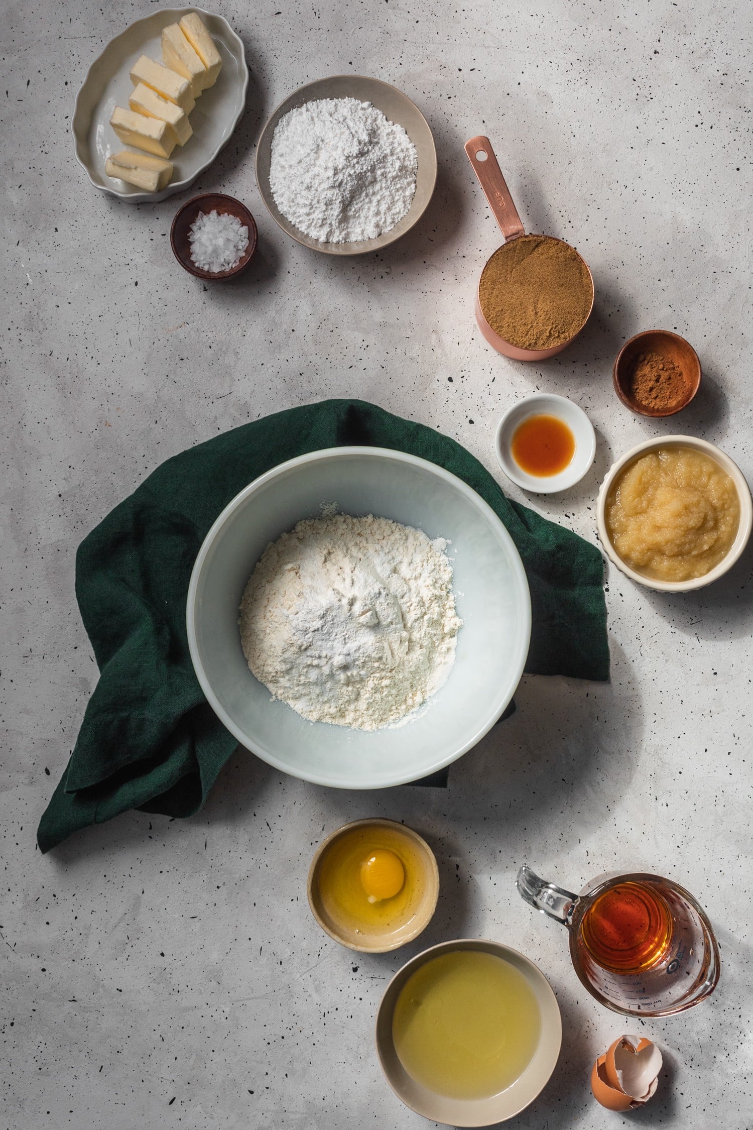 An overhead shot of apple cider whoopie pies ingredients in different white and tan bowls on a grey background.