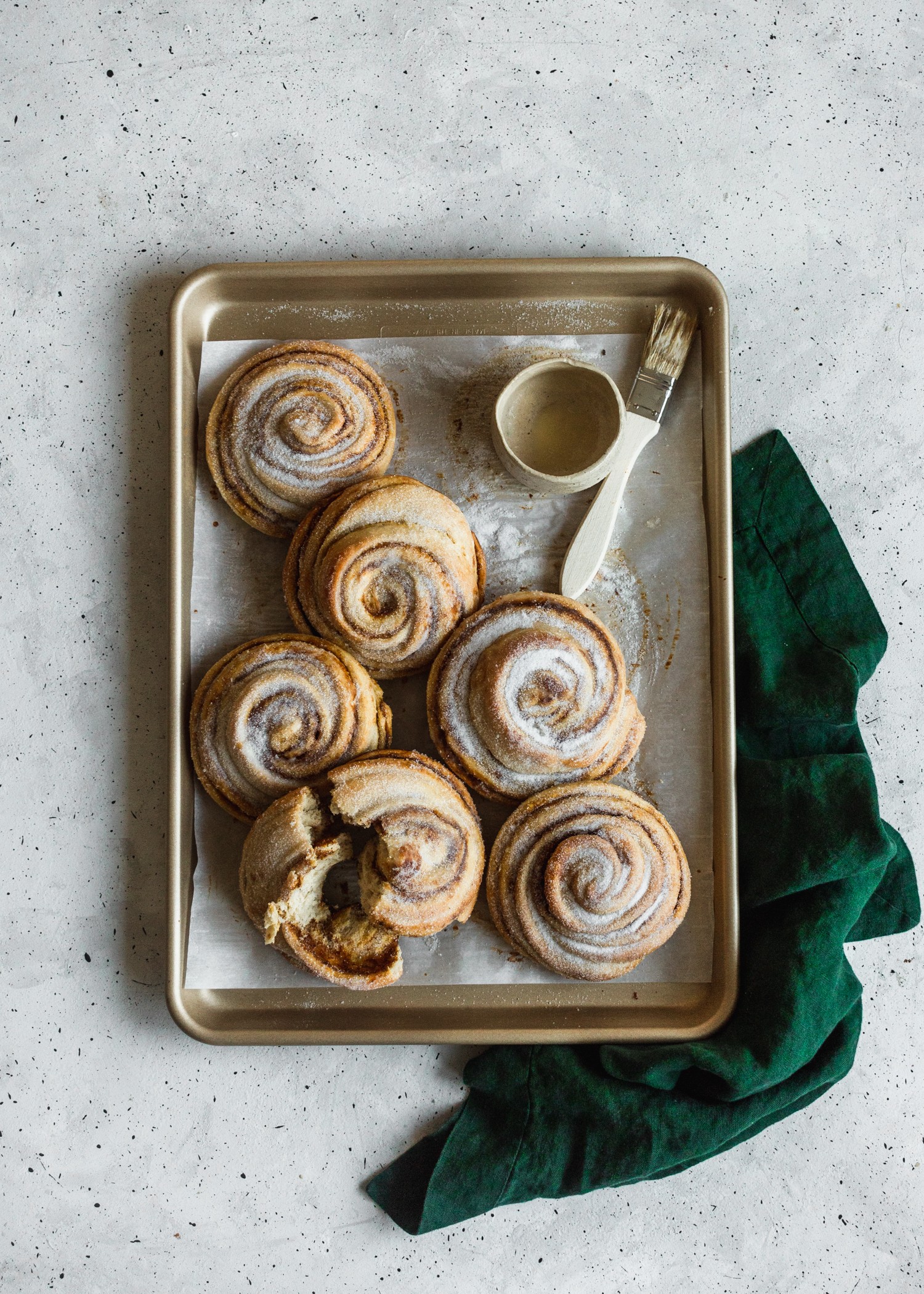 An overhead photo of a gold sheet pan filled with pumpkin morning buns next to a green towel on a grey counter.