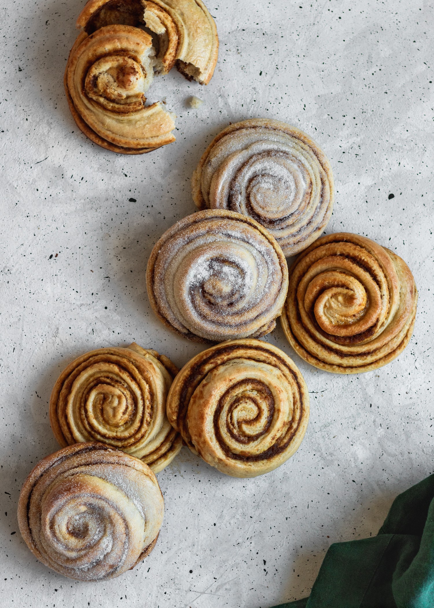 A bird's eye shot of pumpkin morning buns on a speckled white table next to an emerald napkin.