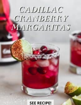 A Cadillac cranberry margarita on a white counter next to limes and Grand Marnier.
