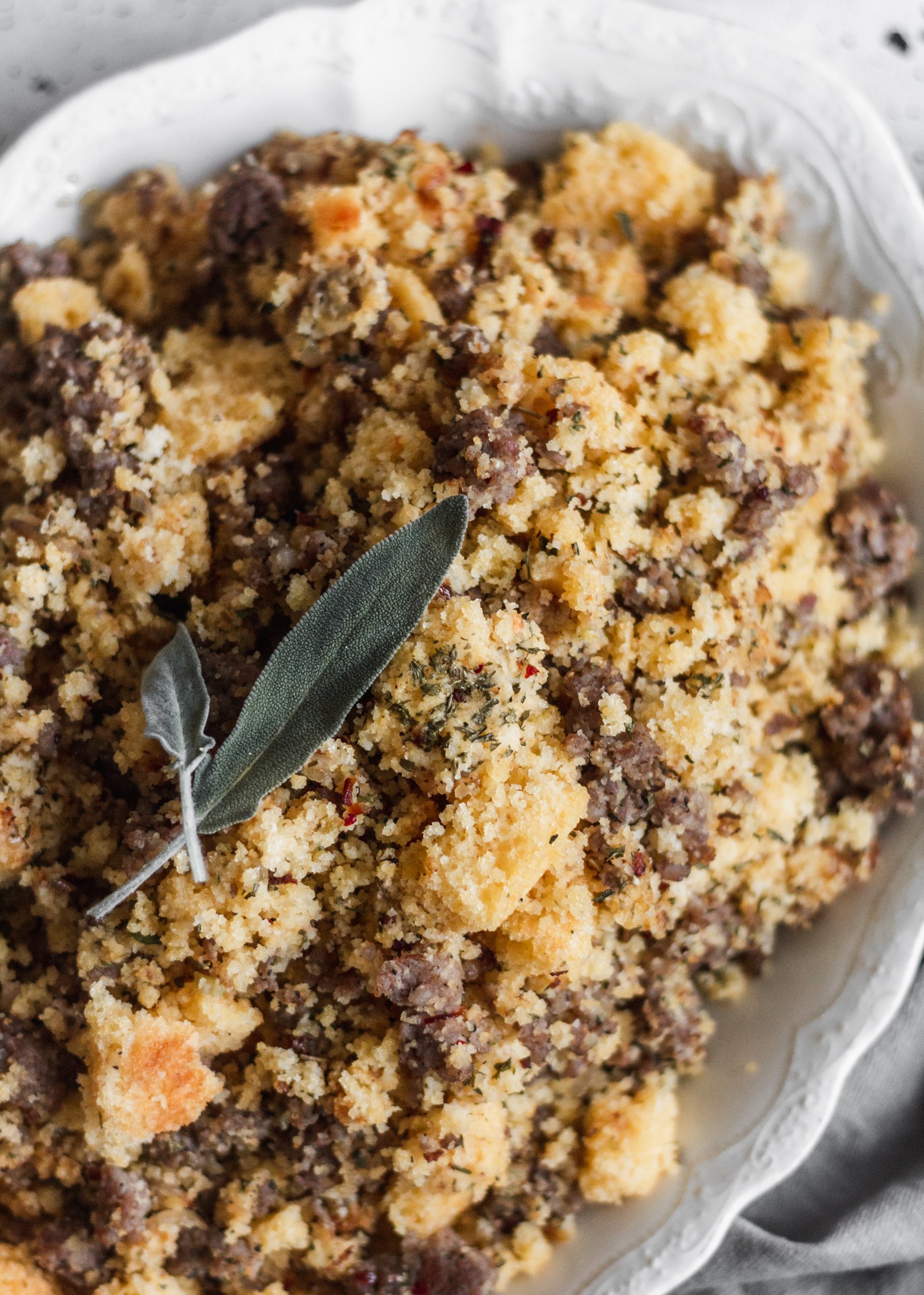 A close-up shot of cornbread stuffing with sausage and sage leaves on top.