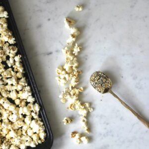 An overhead photo of popcorn on a white marble table next to a gold spoon filled with everything bagel seasoning.