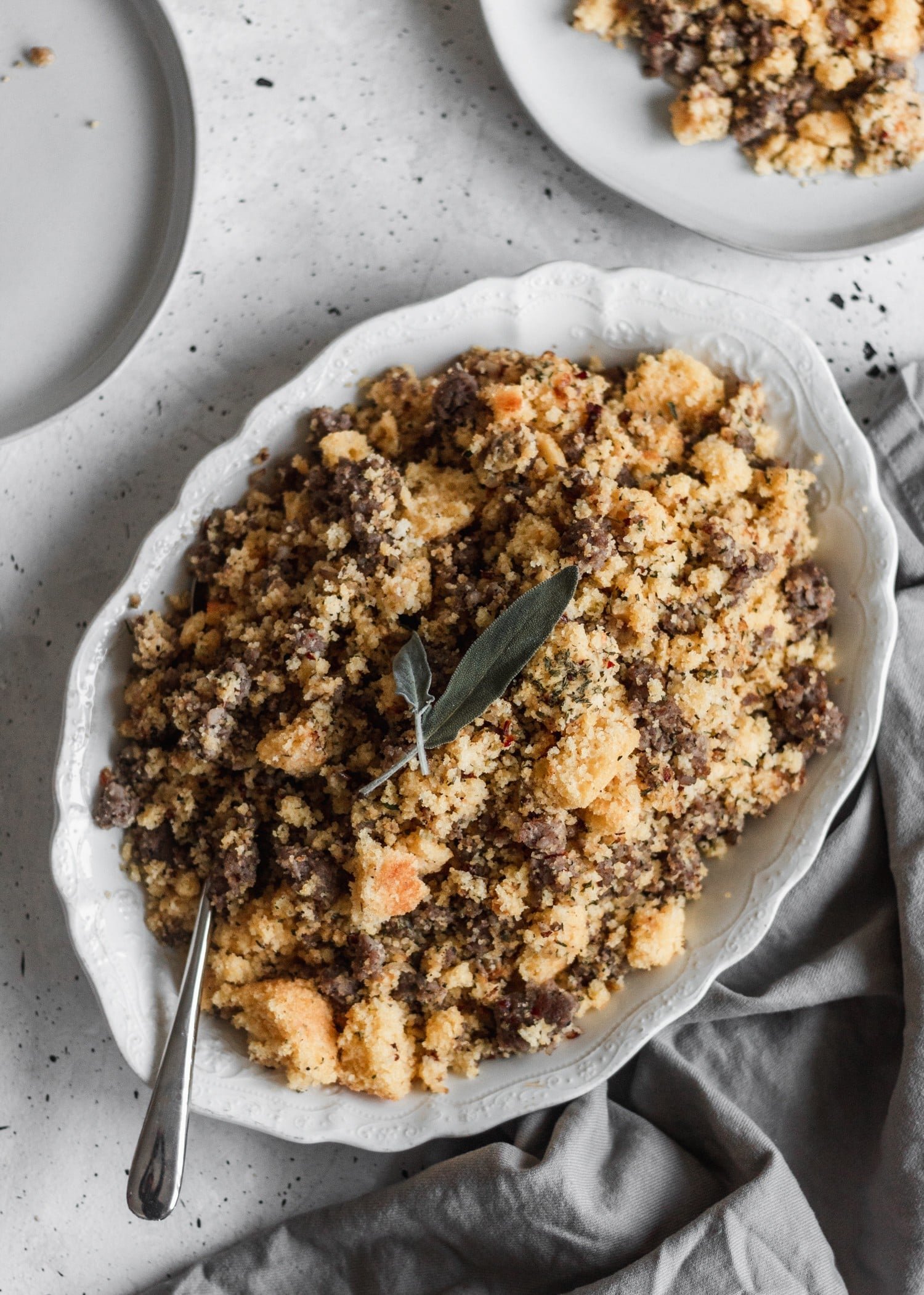 An overhead closeup of cornbread stuffing on an oval white tray sitting on a grey linen.