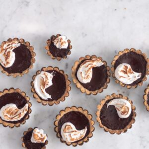 An overhead photo of s'mores tarts on a white marble background.