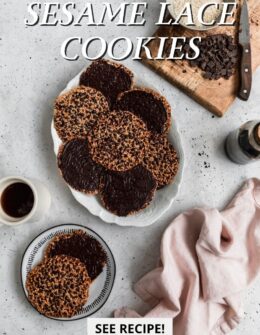 An overhead image of an oval white tray topped with sesame lace cookies on a speckled grey table next to a wood cutting board topped with dark chocolate, a pink linen, a bottle of vanilla, and a cup of coffee.