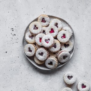 An overhead photo of linzer cookies on a white plate set on a grey table.