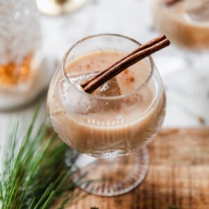 A close up side image of an eggnog White Russian on a wood board with a white background.
