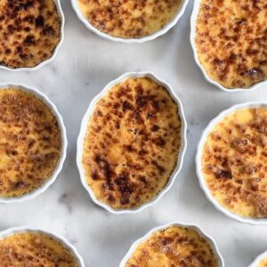 An overhead photo of ramekins filled with creme brulee on a marble table.