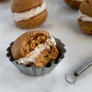 A side image of a whoopie pie with a bite taken out of it placed in a mini tart pan on a white marble background with mjore whoopie pies in the background.