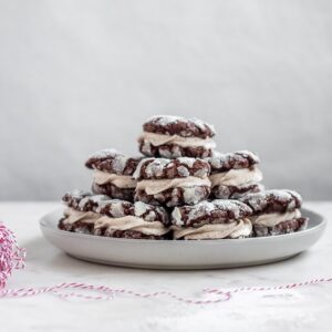 A side image of a plate of cookies on a white marble table next to a roll of red and white striped twine.