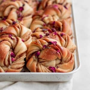 A side image of a row of cardamom buns in a white pan on a marble counter.