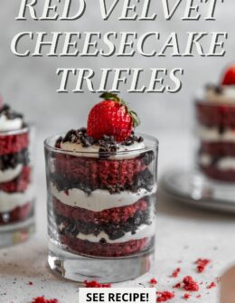 A closeup side image of a red velvet trifle garnished with a strawberry on a grey table with two more trifles in the background.