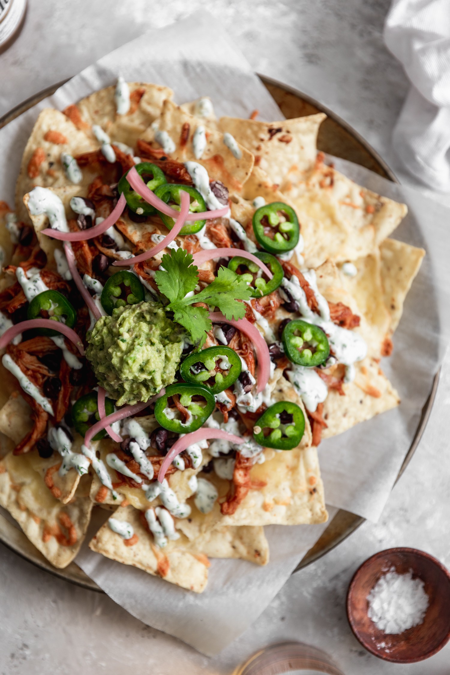 A super closeup overhead photo of tortilla chips topped with cheese, meat, pickled onions, jalapenos, and guacamole on a grey table.