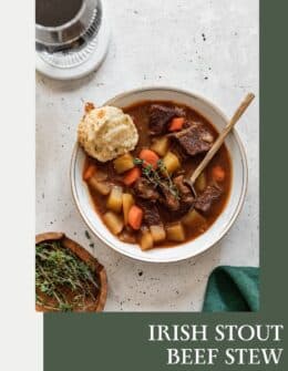 Irish beef stew on a grey counter next to a wood bowl of thyme and an emerald green linen.