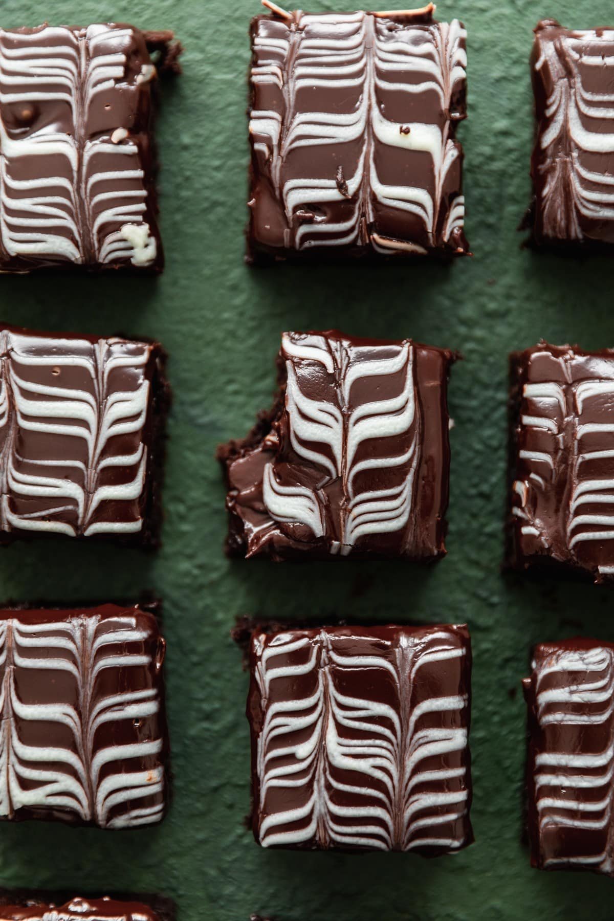 Rows of Irish coffee brownies on a dark green background, with a bite taken out of the middle brownie.