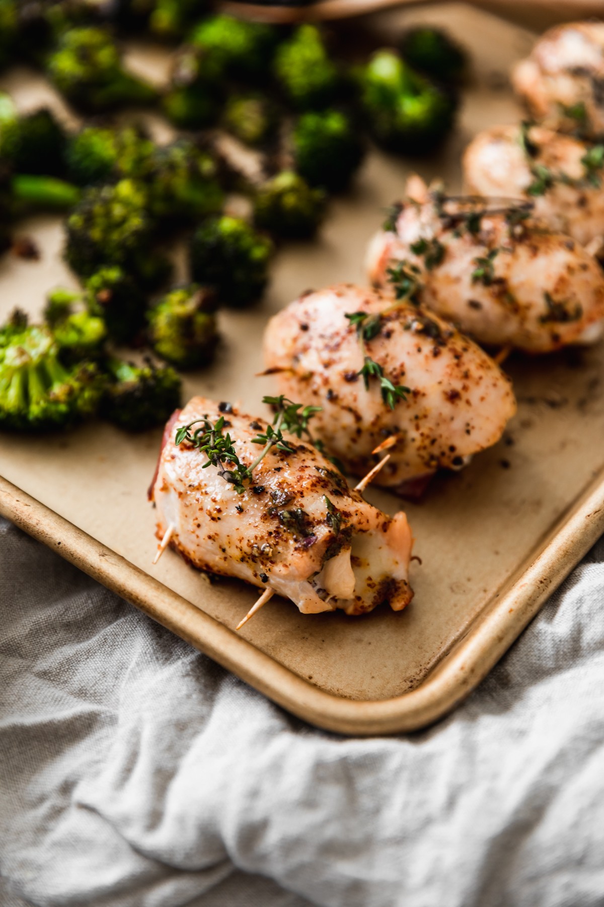A close up side image of a gold sheet pan with rolled chicken and broccoli on a beige linen.