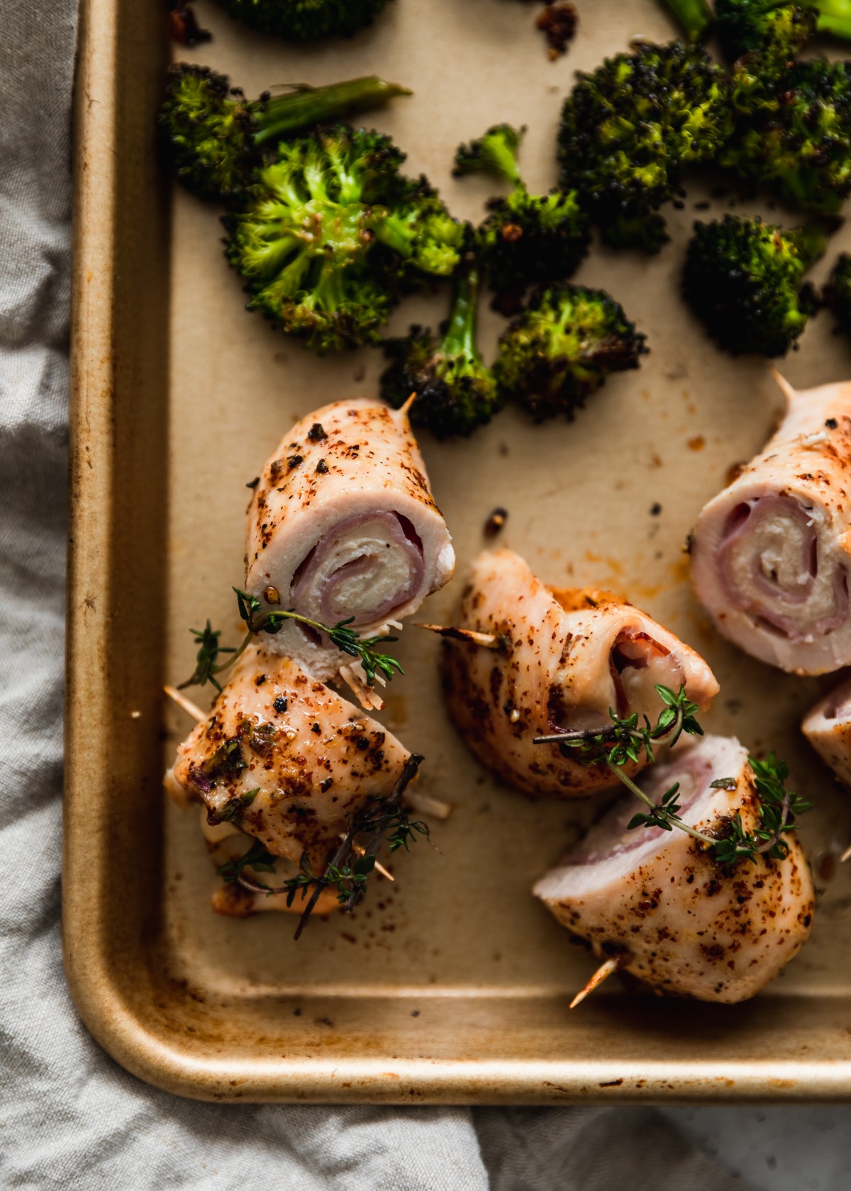 A closeup overhead image of a gold sheet pan topped with roasted broccoli and slices of chicken cordon bleu on a grey counter.