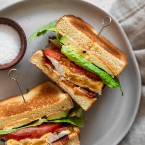 A very closeup overhead image of a halved breakfast BLT on a white plate.