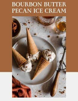 A closeup overhead image of three scoops of bourbon butter pecan ice cream with cones on a white plate next to a vintage ice cream scoop, two glasses of whiskey, and burnt orange linen. The plate is on a white speckled table dusted with chopped pecans.