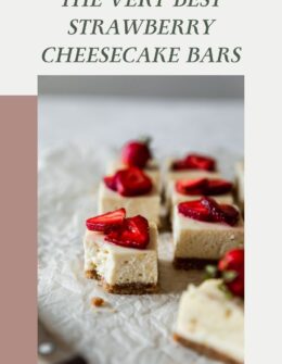 A closeup side image of rows of strawberrry cheesecake bars on white parchment paper. The front bar has a bite taken out of it.