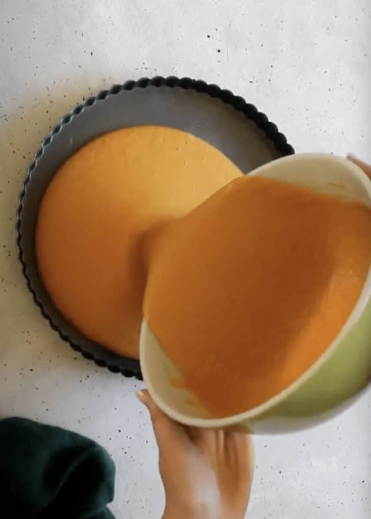 Hands pouring pumpkin filling into a skillet.